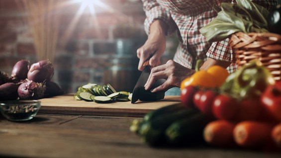 Photo of hands chopping zucchini, with fresh vegetables piled in the right corner of the frame